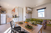 Casa mobile moderna con cucina, tavolo da pranzo per quattro e divano verde al Camping Estival Vendrell Platja.