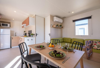 Interior de mobil home moderno con cocina, mesa para cuatro y sofá verde en Camping Estival Vendrell Platja.