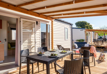 Terrazza coperta con tavolo da pranzo e quattro sedie davanti a casa mobile, Camping Estival Vendrell Platja, Spagna.