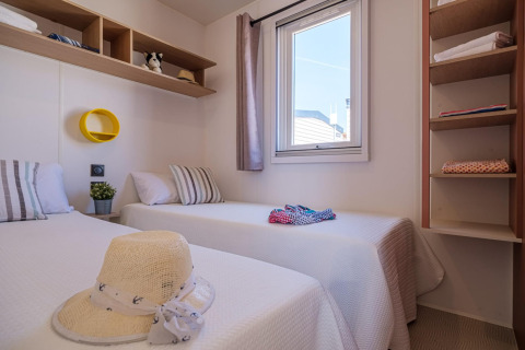 Dormitorio con dos camas individuales, ventana y estantes en mobil home Vendrell Plajta, España.