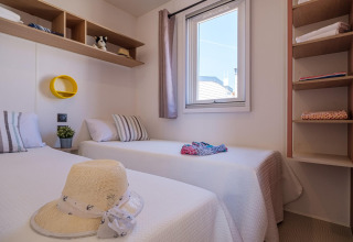 Dormitorio con dos camas individuales, ventana y estantes en mobil home Vendrell Plajta, España.