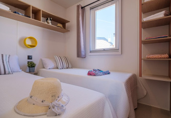 Schlafzimmer mit zwei Einzelbetten, Fenster und Regalen im Mobilheim Vendrell Plajta, Spanien.