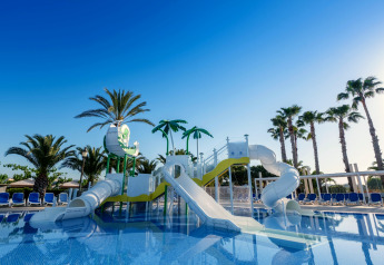 Water playground with slides and palm trees at a glamping accommodation under a clear blue sky.
