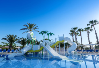 Parco giochi acquatico con scivoli e palme in una struttura glamping sotto un cielo azzurro e limpido.