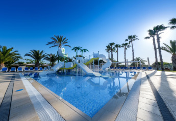 Piscina al aire libre con toboganes y palmeras en CAMPING ESTIVAL VENDRELL PLATJA, casa móvil Mediterránea para 4 personas, España.