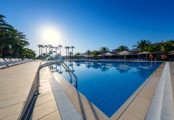 Piscine extérieure dans un hébergement glamping, entourée de palmiers, transats et ciel dégagé.