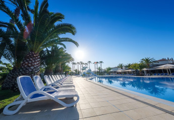 Piscina en alojamiento glamping, rodeada de palmeras y tumbonas bajo un cielo azul despejado.