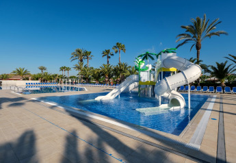 Piscine extérieure avec toboggans et palmiers dans un hébergement glamping sous un ciel bleu clair.