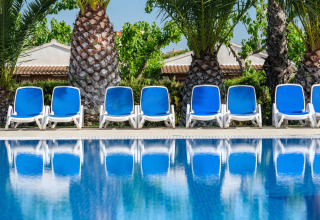 Tumbonas azules junto a una piscina con palmeras en el fondo en Camping Estival Vendrell Platja, España.