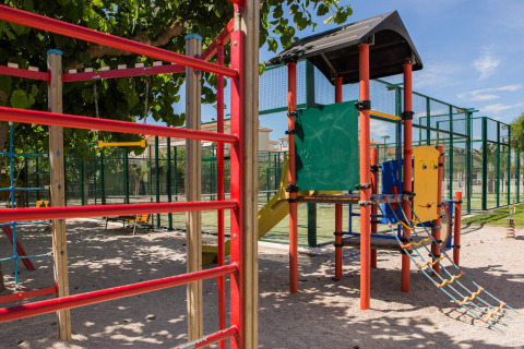 Zona de juegos infantiles con estructura de trepar y tobogán en un glamping con canchas deportivas.