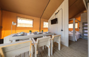 Innenansicht eines luxuriösen Safari-Zeltes mit Essbereich, Schlafzimmer und Holzmöbeln in Spanien.
