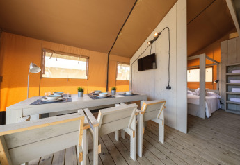 Innenansicht eines luxuriösen Safari-Zeltes mit Essbereich, Schlafzimmer und Holzmöbeln in Spanien.