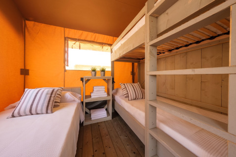 Indvendig udsigt over et Grand Safari glamping telt med køjesenge, enkelt senge og orange vægge.
