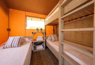 Vue intérieure d'une tente Grand Safari Glamping avec lits superposés, lits simples et murs orange.