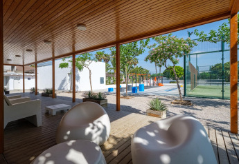 Outdoor-Loungebereich im Camping Estival Vendrell Platja Tent Grand Safari Glamping in Spanien mit moderner Sitzgelegenheit, Bäumen und Sportplatz im Hintergrund.