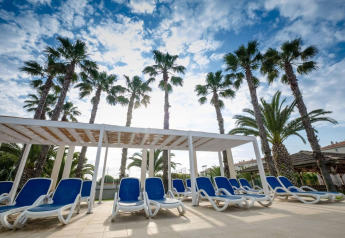 Transats bleus sous pergola bordée de palmiers au Camping Estival Vendrell Platja Grand Safari Glamping, Espagne.