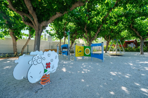 Legeplads med får-figur, gynger og træer i skyggefuldt område i Spanien, Camping Estival Vendrell Platja.
