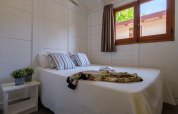 Lichte slaapkamer met tweepersoonsbed, gestreepte kussens, raam en plant bij Camping Estival Vendrell Platja, Spanje.