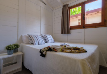 Lichte slaapkamer met tweepersoonsbed, gestreepte kussens, raam en plant bij Camping Estival Vendrell Platja, Spanje.