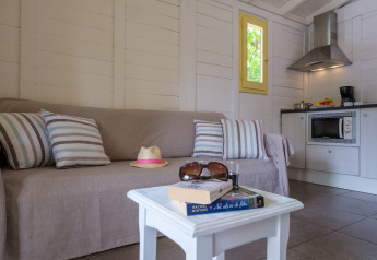 Woonruimte in een bungalow met bank, gestreepte kussens, salontafel met boeken en open keuken.