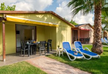 Vue extérieure d’un bungalow jaune avec terrasse, transats et palmier au Camping Estival Vendrell Platja en Espagne.