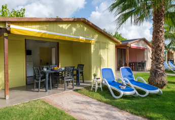 Buitenaanzicht van een gele bungalow met terras, ligstoelen en palm bij Camping Estival Vendrell Platja in Spanje.