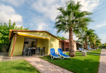 Bungalows colorés au Camping Estival Vendrell Platja avec palmiers, chaises longues et pelouse verte.
