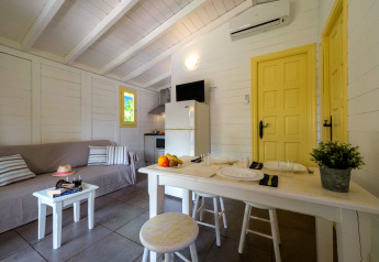 Vue intérieure d’un bungalow avec canapé, table à manger, cuisine et portes jaunes au Vendrell Platja Camping en Espagne.