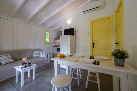 Indvendig udsigt over bungalowlokale med sofa, spisebord, køkken og gule døre på Vendrell Platja Camping i Spanien.