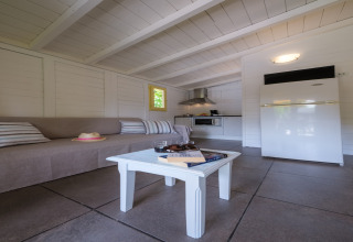 Indvendigt billede af en lys bungalow med sofa, sofabord, køkken og køleskab på Vendrell Platja i Spanien.