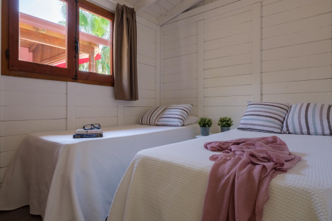 Lyst bungalowværelse med to enkeltsenge, planter og vindue hos CAMPING ESTIVAL VENDRELL PLATJA i Spanien.