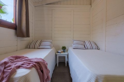 Indretning af et lyst værelse med to enkeltsenge, stribede puder, vindue og natbord i en bungalow.