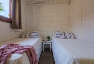 Indretning af et lyst værelse med to enkeltsenge, stribede puder, vindue og natbord i en bungalow.