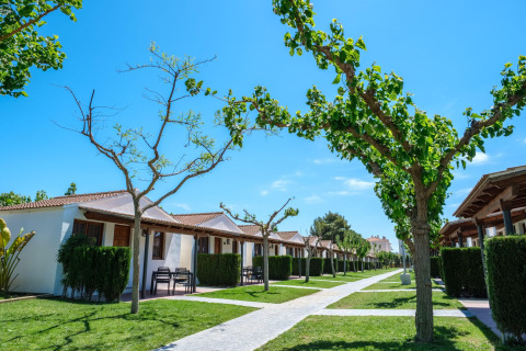 Række af bungalows på CAMPING ESTIVAL VENDRELL PLATJA under en klar blå himmel i Spanien med grønne træer.