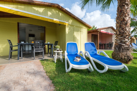 To blå solstole, et bord og stole foran en gul bungalow på CAMPING ESTIVAL VENDRELL PLATJA i Spanien.