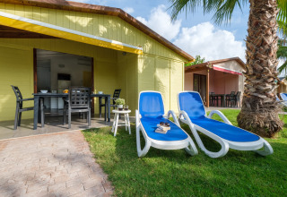 To blå solstole, et bord og stole foran en gul bungalow på CAMPING ESTIVAL VENDRELL PLATJA i Spanien.