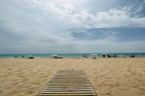Strandfoto taget ved Camping Estival Vendrell Platja i Spanien med træsti, sand, parasoller og hav.