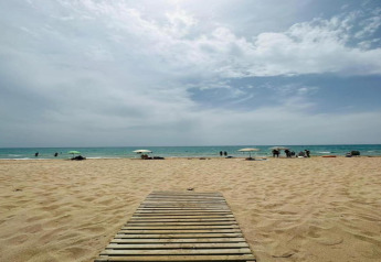 Strandbeeld bij Camping Estival Vendrell Platja, Spanje, met houten pad, parasols, zand en zee.