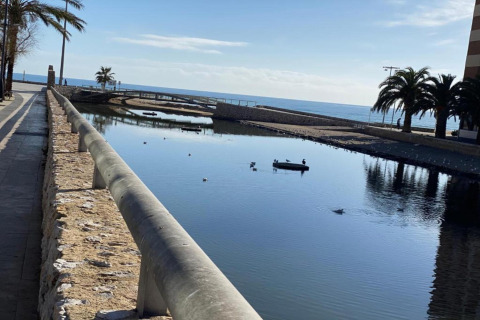 Udsigt over kanal med små broer, palmer og hav i baggrunden ved Camping Estival Vendrell Platja i Spanien.