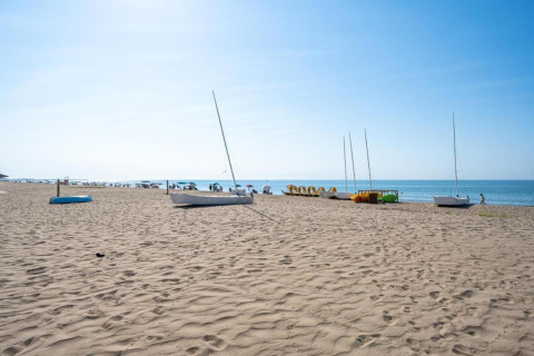 Strandsceneri ved Camping Estival Vendrell Platja i Spanien med både, parasoller og klar blå himmel.