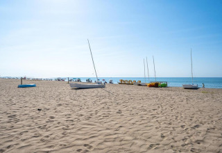Strandsceneri ved Camping Estival Vendrell Platja i Spanien med både, parasoller og klar blå himmel.