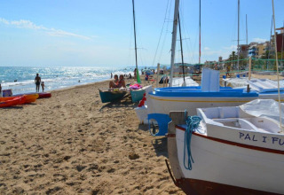 Sandstrand med både og mennesker ved Camping Estival Vendrell Platja Bungalow 4 Standard i Spanien.