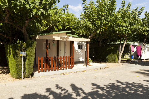 Mobilhome ved Camping Cambrils Playa BUNGALOW OHARA i Spanien, omgivet af træer og grønne hække.
