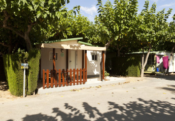 Stacaravan bij Camping Cambrils Playa BUNGALOW OHARA in Spanje, omgeven door bomen en groene hagen.