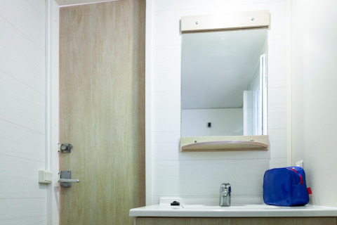 Badeværelse i mobilhome ved Camping Cambrils Playa med spejl, vask og en blå toiletmappe på bordet.