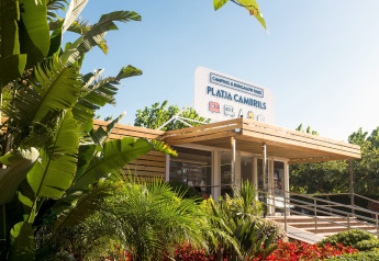 Entrance to Camping & Bungalow Park Platja Cambrils in Spain, surrounded by lush green tropical plants.