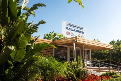 Indgangen til Camping & Bungalow Park Platja Cambrils i Spanien, omgivet af frodige grønne planter.