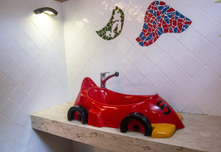 Lavabo con forma de coche de carreras rojo sobre encimera de piedra, foto tomada en alojamiento glamping.