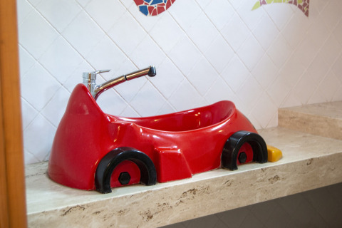 Lavabo rojo en forma de coche en un baño de glamping, colocado sobre una encimera de mármol beige.