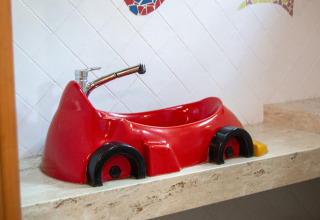 Lavabo rojo en forma de coche en un baño de glamping, colocado sobre una encimera de mármol beige.
